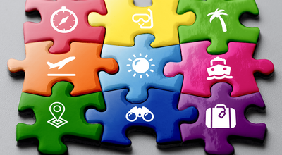 Neun bunte Puzzle-Teile auf grauem Hintergrund, jedes Puzzle-Teil hat ein anderes weißes Symbol (Kompass, Taucherbrille, Palme, Flugzeug, Sonne, Schiff, Map-Pin, Fernglas und Koffer).